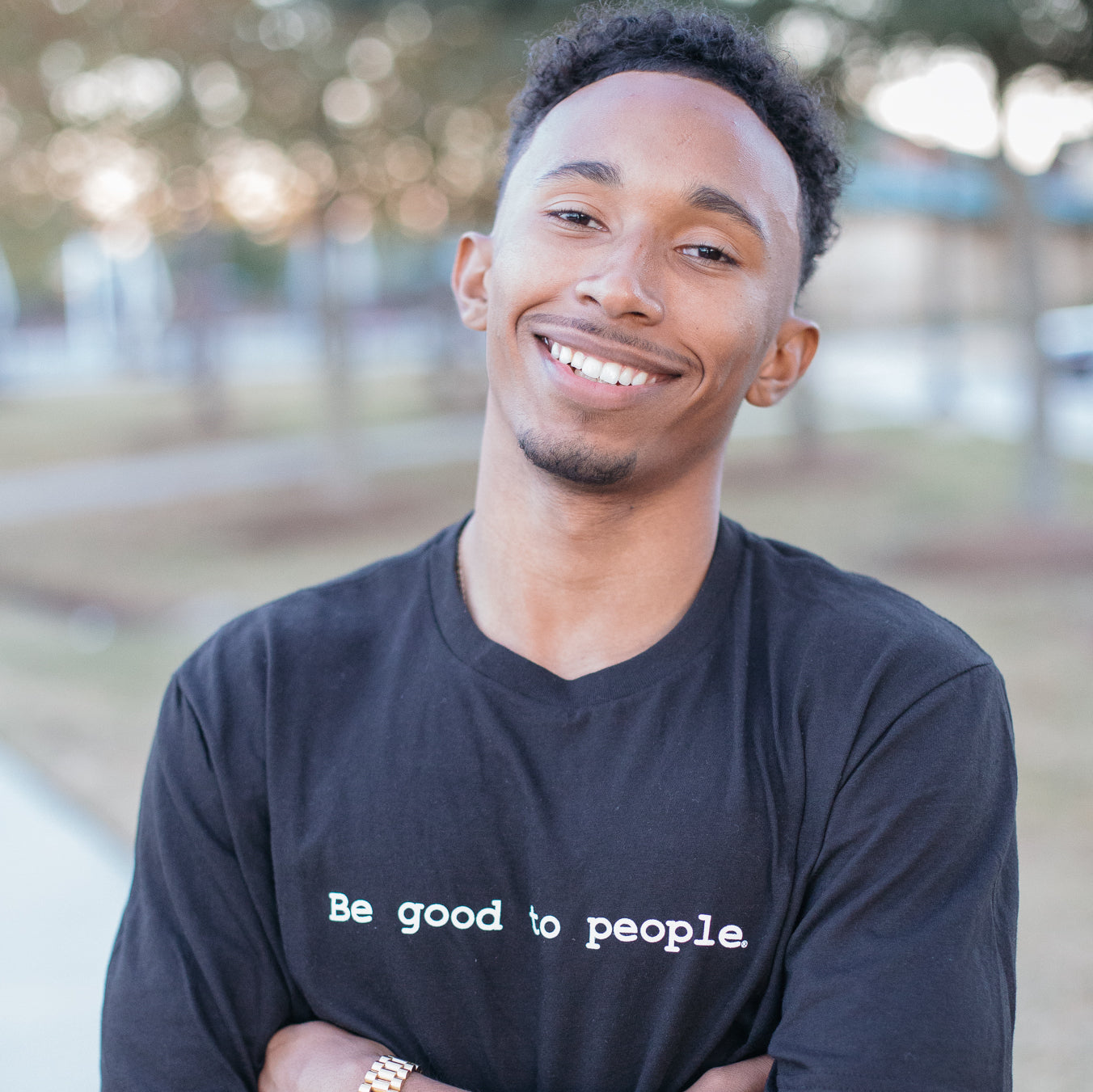 Man standing with his arms crossed wearing a Be Good to People long sleeve shirt.