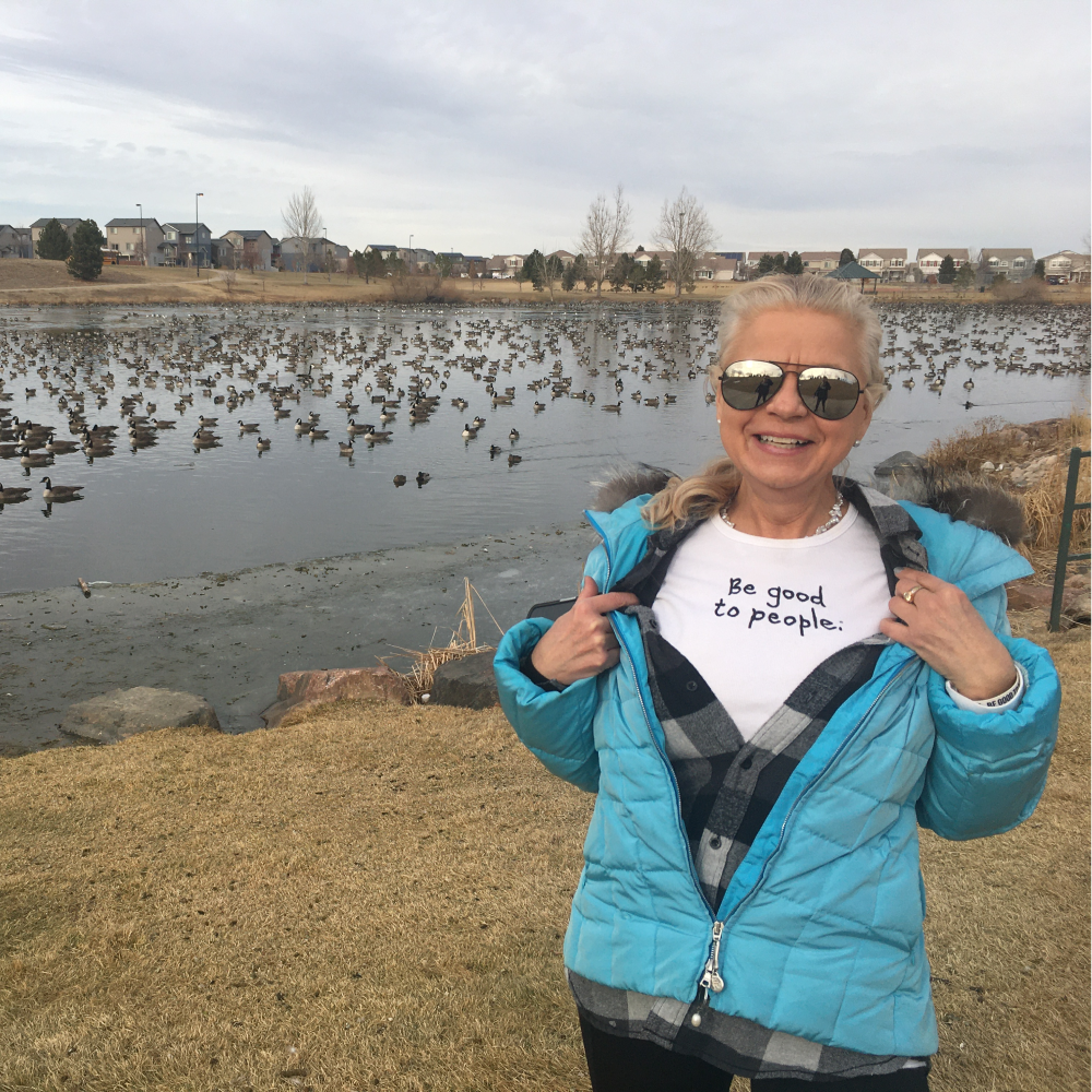 Older woman at a duck pond wearing a Be Good to People Tshirt
