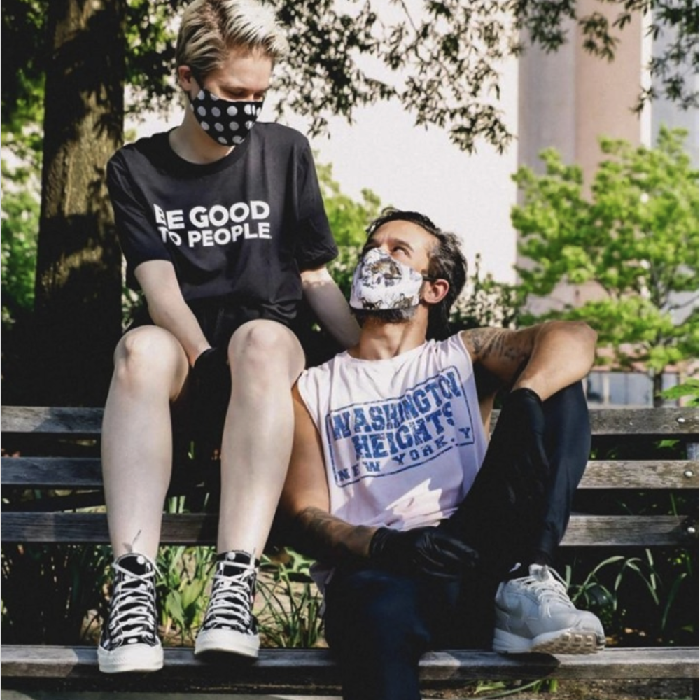 Two people on a park bench. One sitting on the backrest with a Be Good to People shirt.