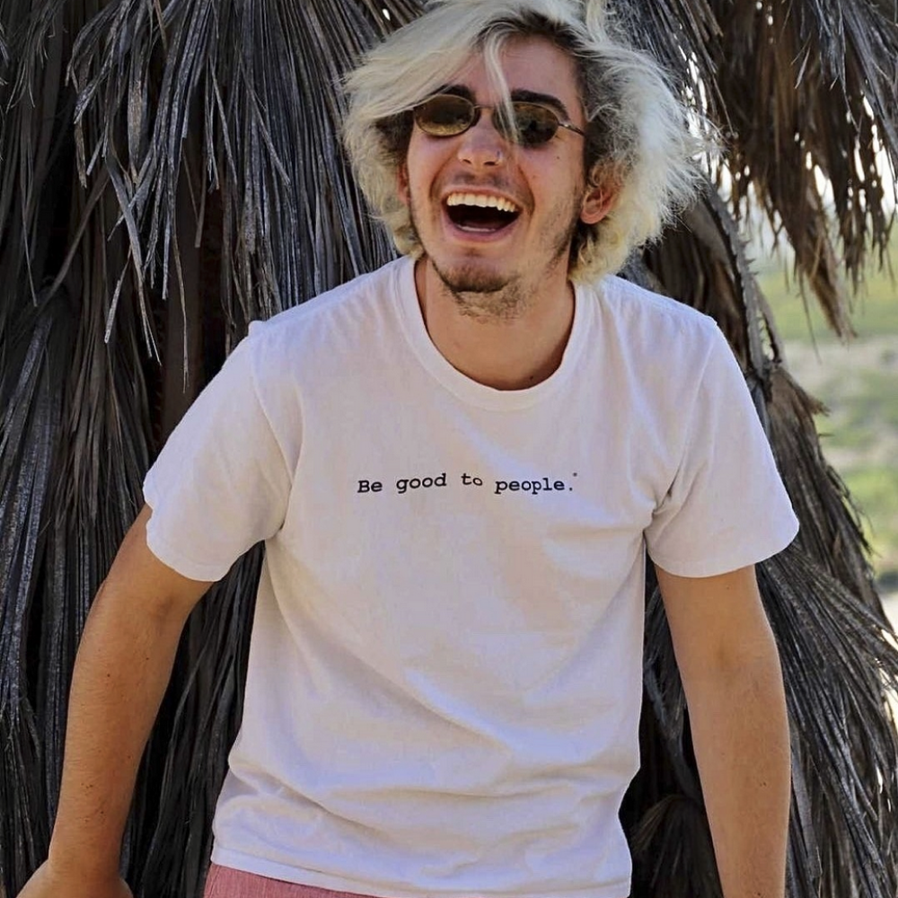 Person laughing against a palm like tree with a Be Good to People t shirt